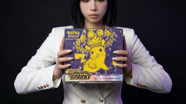 Pokemon Surging Sparks Pokemon Center Elite Trainer Box held by the Evol Vault content host in editorial product photography on a dark studio backdrop