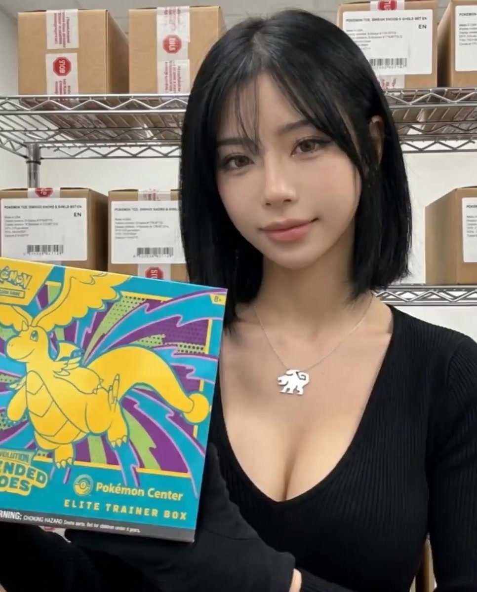 Alice, Evol Vault content editor, holding a sealed Ascended Heroes Pokémon Center Elite Trainer Box, sealed Pokémon TCG products on shelving behind.